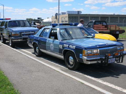 2001 Ford Crown Victoria - A Massachusetts State Police car is parked alongside other vehicles on a sunny day.