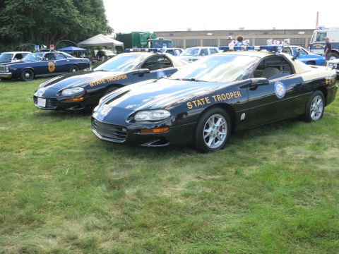 2001 Ford Crown Victoria - Two black Chevrolet Camaros, marked as State Trooper vehicles, are parked on a grassy field.