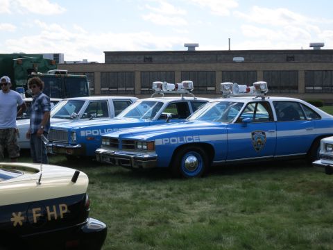 2001 Ford Crown Victoria - Several police cars are parked on a grassy field in front of a brick building.