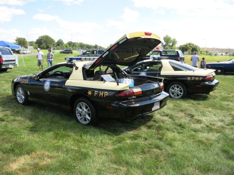 2001 Ford Crown Victoria - Two police cars, one with its trunk and hood open, are parked on a grassy field.