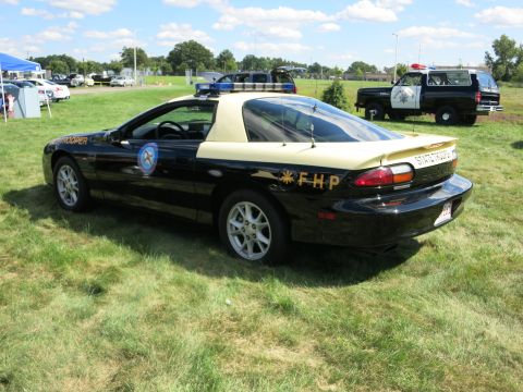 2001 Ford Crown Victoria - A police car, possibly a Chevrolet Camaro, is parked on a grassy field with another police vehicle in the background.