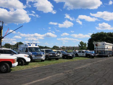 2001 Ford Crown Victoria - A variety of emergency vehicles, including police cars and an ambulance, are parked in a line on a sunny day.