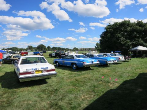 2001 Ford Crown Victoria - A collection of vintage police vehicles are displayed outdoors under a bright, cloudy sky.