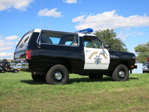 2001 Ford Crown Victoria - A black and white police SUV with a light bar is parked on a grassy field under a blue sky with clouds.