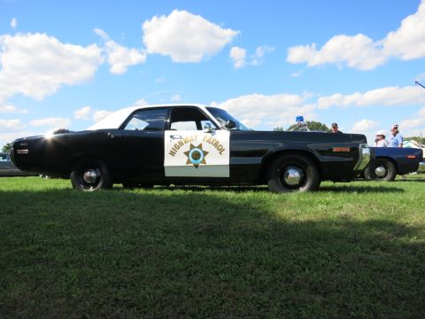 2001 Ford Crown Victoria - A classic black and white patrol car sits on grass under a cloudy sky, with another vehicle partially visible behind it.