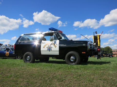 2001 Ford Crown Victoria - A Dodge Ramcharger SUV painted as a Highway Patrol vehicle sits on grass under a blue sky with clouds.