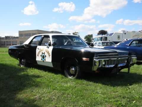 2001 Ford Crown Victoria - A vintage black and white highway patrol car is parked on a grassy field under a partly cloudy sky.