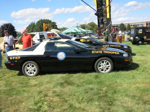 2001 Ford Crown Victoria - Two black and white police cars are parked on a grassy field under a blue sky with scattered clouds.