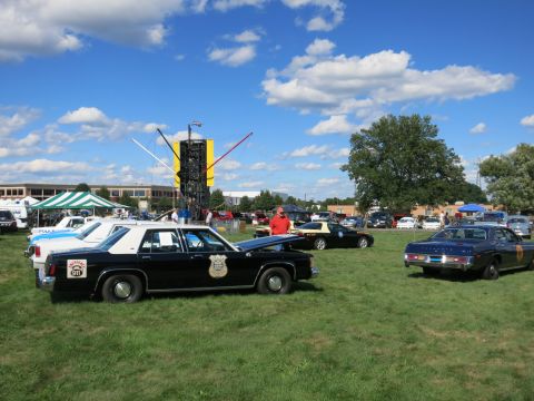 2001 Ford Crown Victoria - Multiple police vehicles are displayed at an outdoor event with a large metal sculpture in the background.