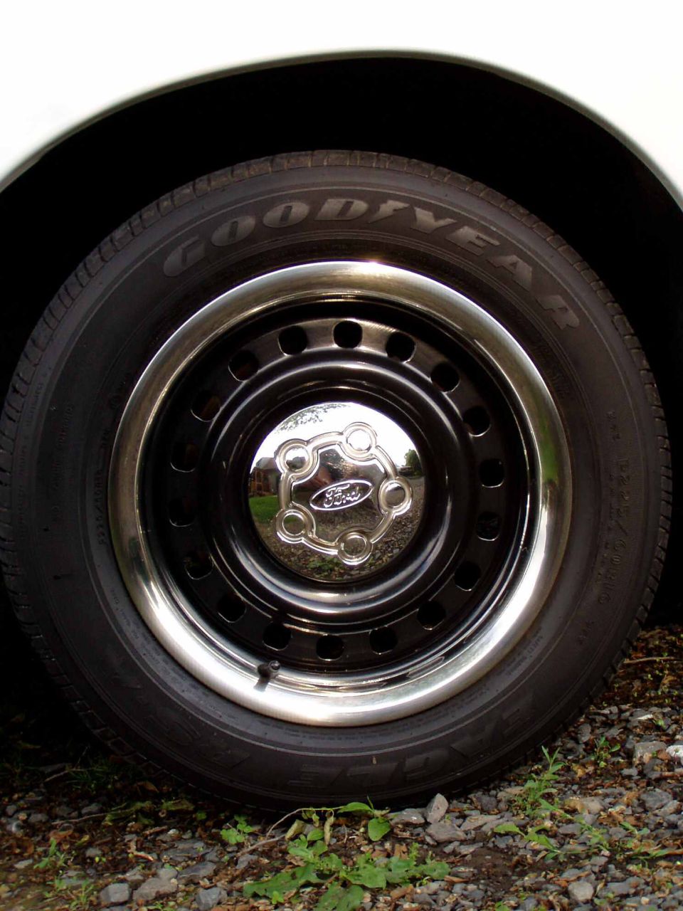 Close-up of a black steel wheel with a chrome trim ring and a Ford-branded hubcap. Goodyear tire visible