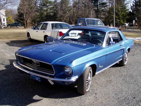 1999 Ford Crown Victoria - A blue 1967 Ford Mustang coupe is parked in front of a white sedan and a blue pickup truck.