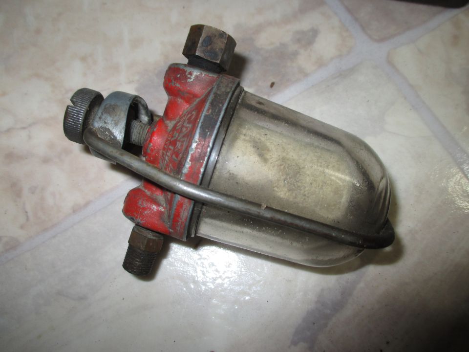 Red and metal fuel filter with a glass bowl. It has a metal clamp and threaded fittings