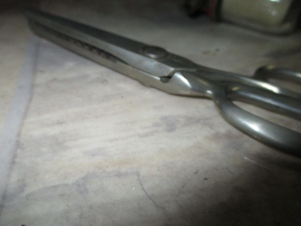 Metal scissors with serrated blades and looped handles resting on a textured surface