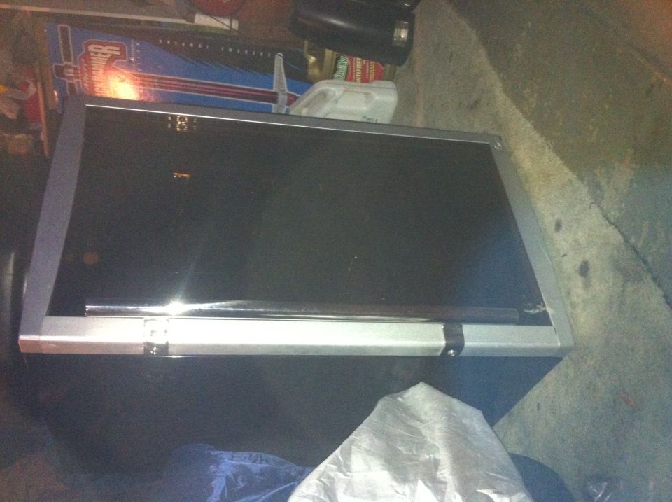 Black tool chest with silver trim, sitting on a concrete floor. Some blue and red graphics are visible in the background