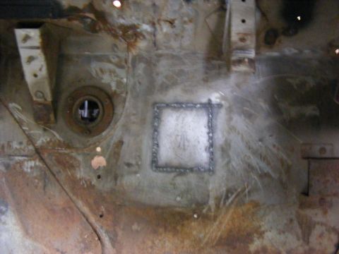 Close-up of a square metal patch welded onto a rusty, weathered surface with circular fittings