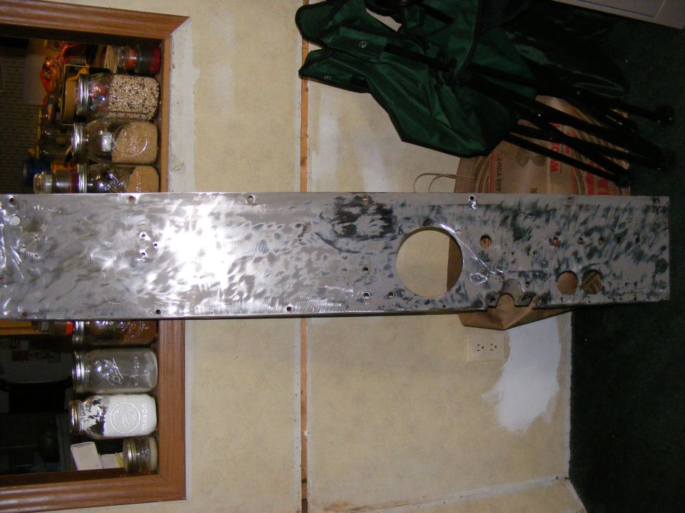 Bare metal panel with circular and smaller holes, mounted on a wall