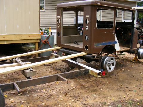 Brown truck cab with missing doors and windows, resting on a trailer frame with wooden supports