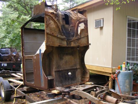 rusted vehicle cab on trailer, next to a shed