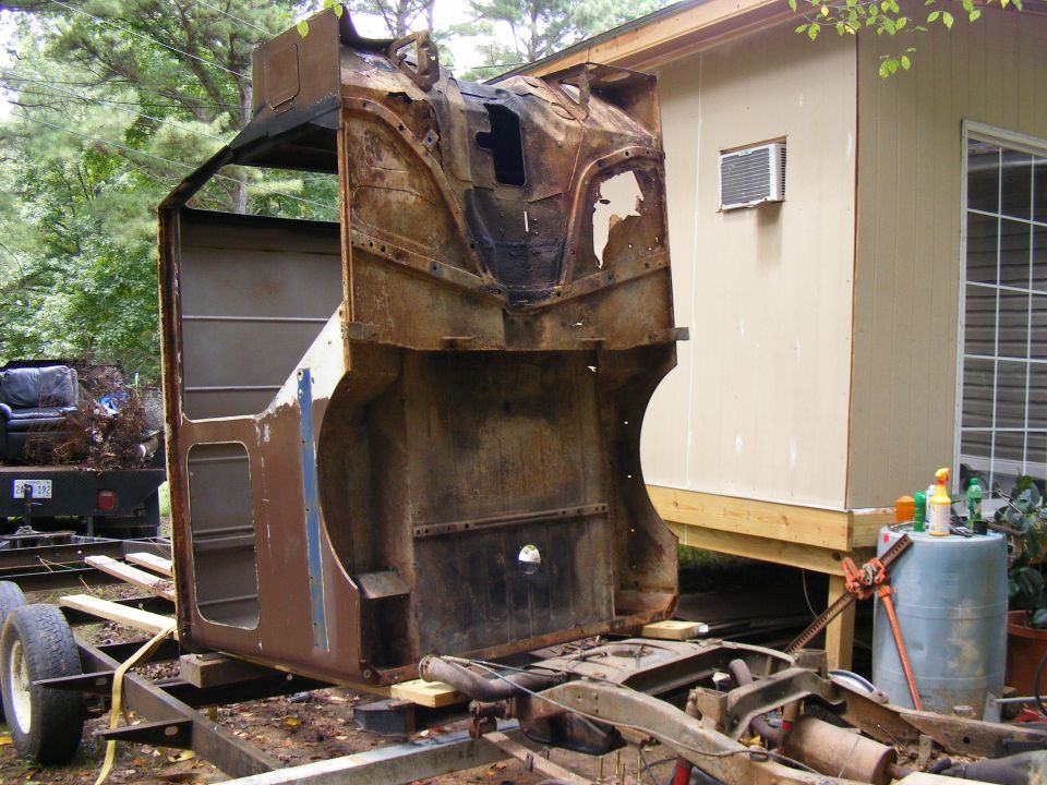 rusted vehicle cab on trailer, next to a shed