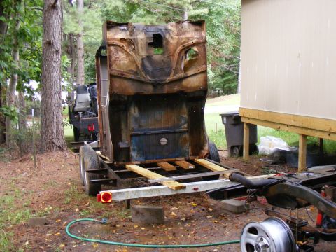Rusted vehicle body on trailer, rear view. Another vehicle visible behind