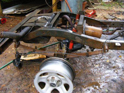 Vehicle frame with suspension components and a detached wheel. Looks like it's in a yard
