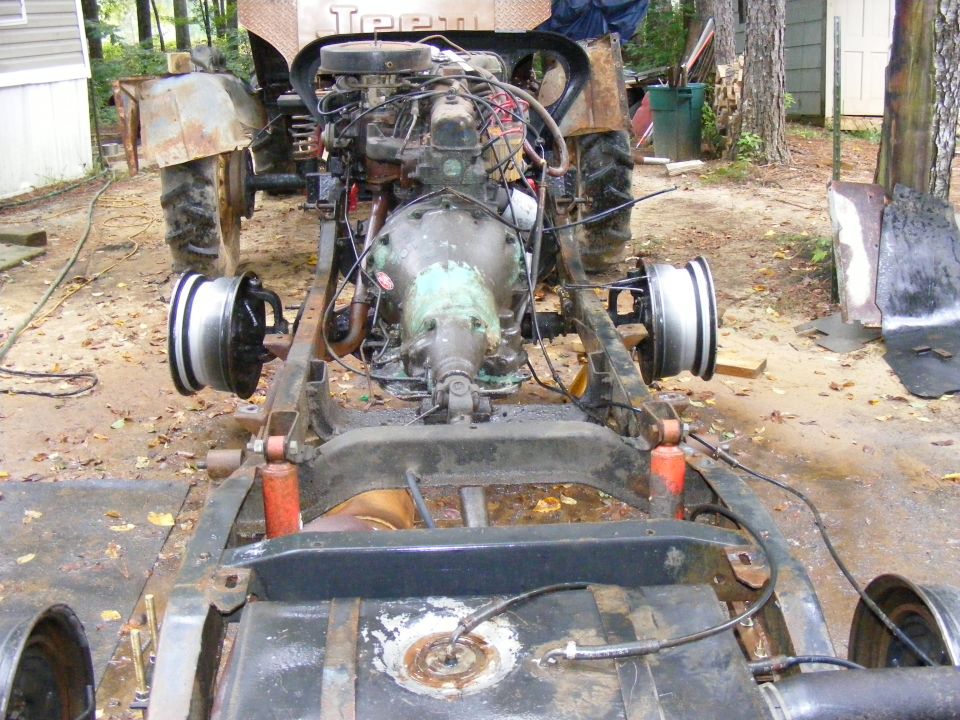 Vehicle chassis with engine and transmission, front view. SuperMotors.net logo visible