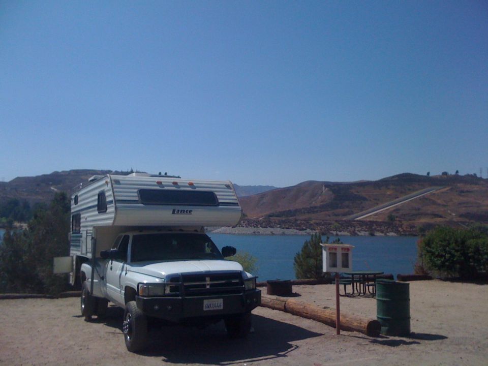 White pickup truck with a Lance camper shell parked at a campsite overlooking a lake