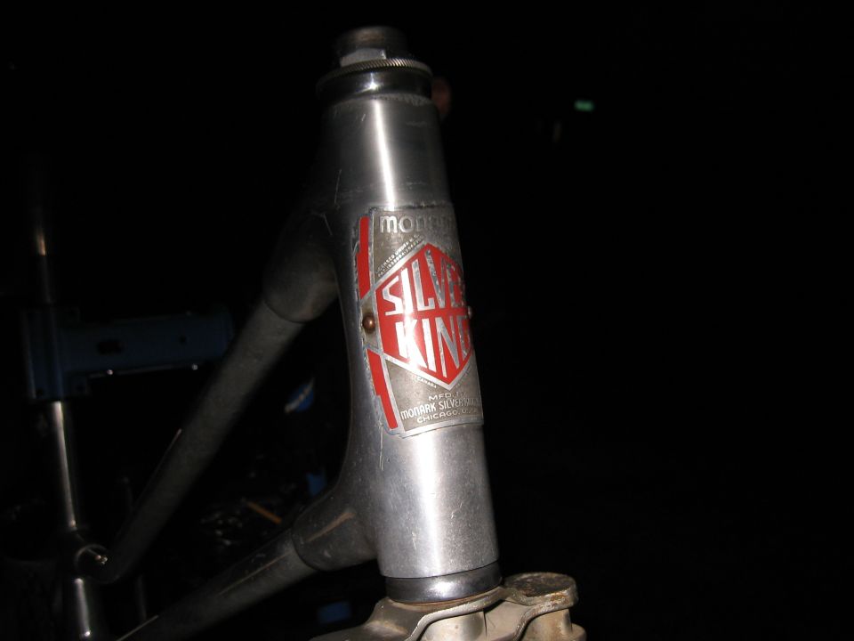 Close-up of a silver bicycle head tube with a red and silver 'Silver King' badge. Text below says 'MFG. BY MONARK SILVER KING CHICAGO'
