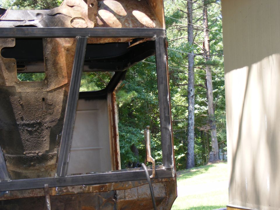 Rusted vehicle frame with welded metal supports, showing interior paneling and exterior trees
