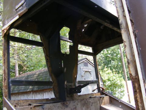Interior of a rusty vehicle with exposed frame and a shed in the background