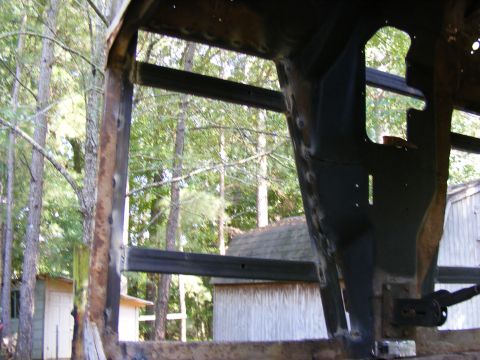 rusted metal frame of a vehicle, viewed from inside, with trees and buildings in background
