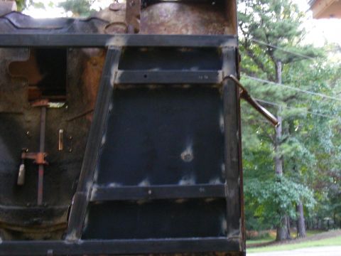 Vehicle frame with welded metal plates and a metal bracket. Rusty metal and dark panels are visible