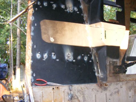 Close-up of a black vehicle body panel with numerous weld spots and a pair of pliers. Some rust is visible on