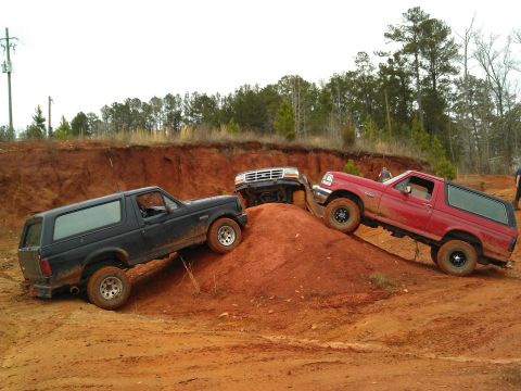 1992 Ford Bronco - Multiple Ford Broncos navigate a challenging off-road course with steep inclines and loose dirt.