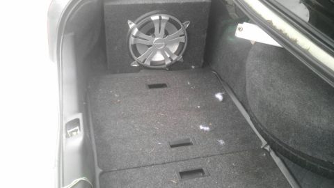 2000 Mercury Grand Marquis - The trunk of a vehicle features a custom subwoofer enclosure and carpeted floor, with a spare tire visible on the right.
