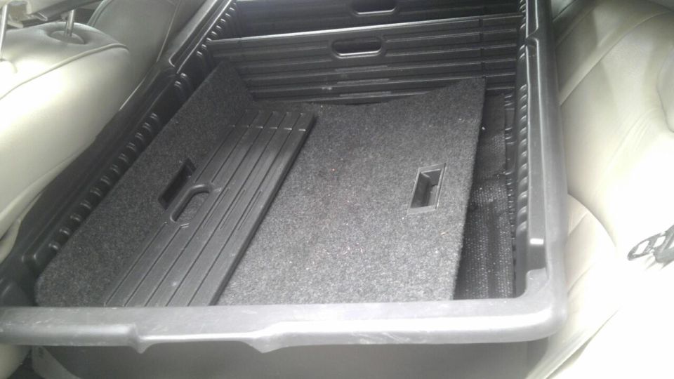 Car trunk interior showing a plastic organizer with carpeted floor and side panels. Rear seats are visible