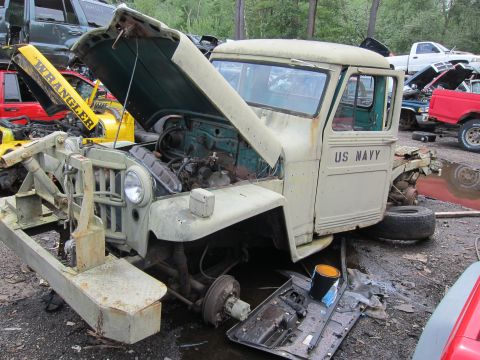 2001 Ford Crown Victoria - A weathered US Navy Jeep sits in a junkyard with its hood open, revealing the engine compartment.