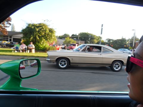 1971 Ford Ranchero - A tan 1967 Ford Galaxie 500 Fastback is seen driving on a sunny day, with people sitting on chairs in the background.