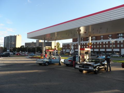 1971 Ford Ranchero - Several cars are parked at gas pumps under a canopy on a sunny day.