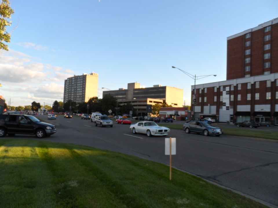 White 1975 Pontiac Firebird driving on a street with buildings and other cars