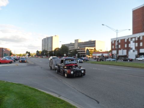 1971 Ford Ranchero - A heavily modified pickup truck tows a trailer down a city street with other vehicles and buildings in the background.