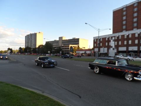 1971 Ford Ranchero - A black station wagon with flame decals drives down the road past buildings.