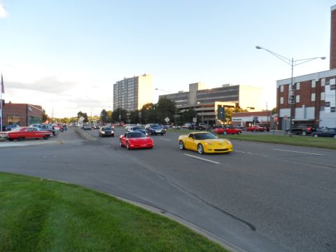 1971 Ford Ranchero - A yellow Chevrolet Corvette cruises down a street alongside other vehicles under a clear sky.