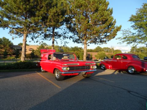 1971 Ford Ranchero - Two classic red vehicles are parked in a lot with trees and a building in the background.