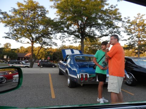 1971 Ford Ranchero - Two people stand next to a blue muscle car with white racing stripes in a parking lot.