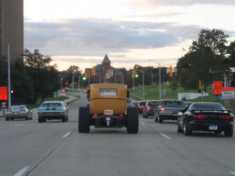 1971 Ford Ranchero - A yellow hot rod truck with massive rear tires drives in traffic on a cloudy day.