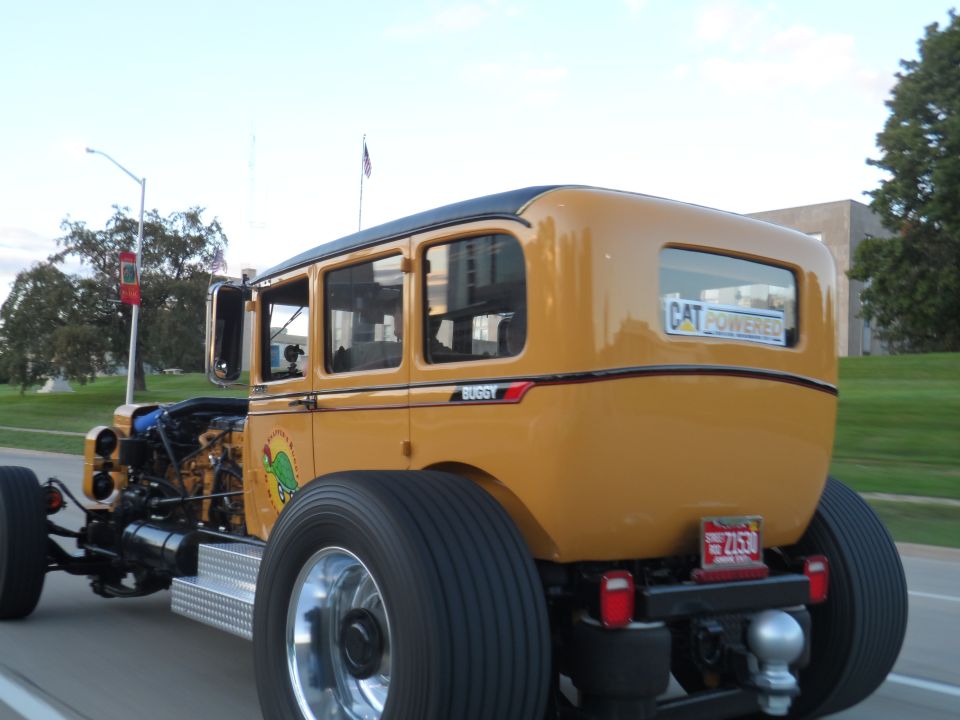 Yellow custom hot rod with exposed engine, large rear tires, and "CAT POWERED" sticker