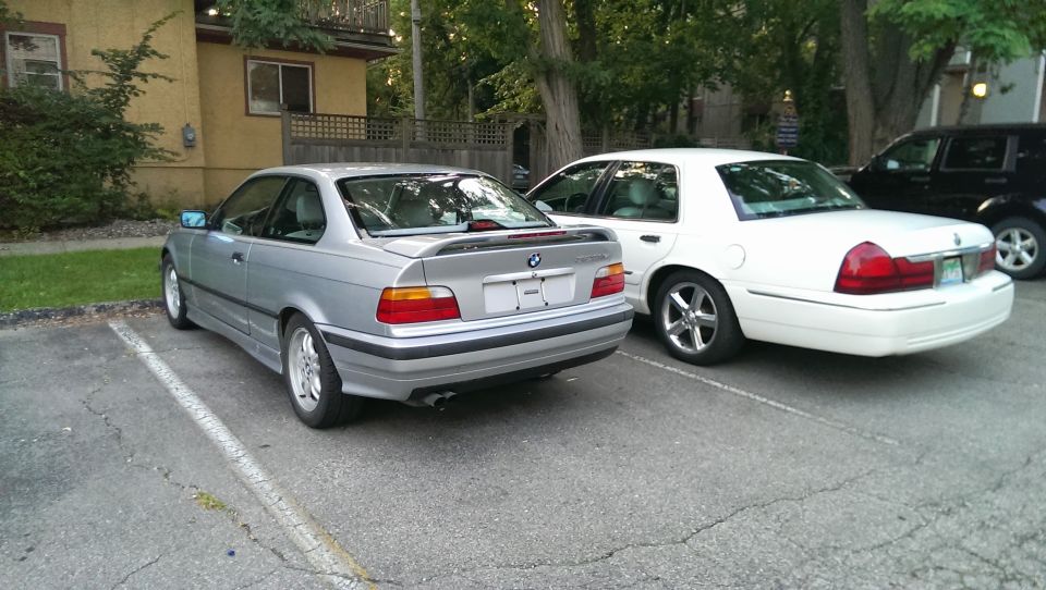 Silver BMW 3 Series coupe parked in a lot, rear view. Spoiler on trunk