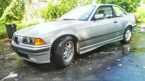 1997 BMW 3 Series - A silver BMW 3 Series coupe is parked outside on a wet surface with greenery in the background.