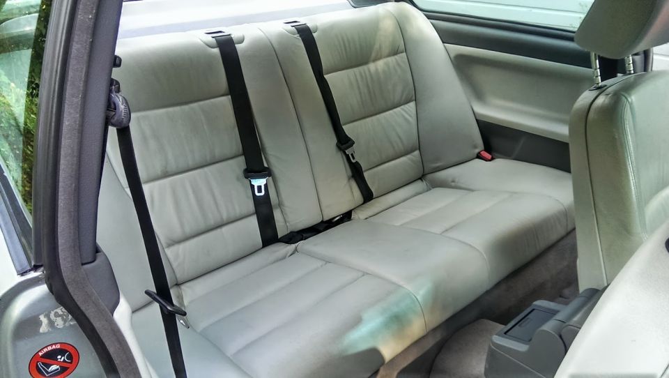 Light gray leather rear seats with black seatbelts inside a car